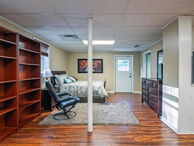 bedroom featuring a drop ceiling, visible vents, baseboards, ornamental molding, and dark wood finished floors