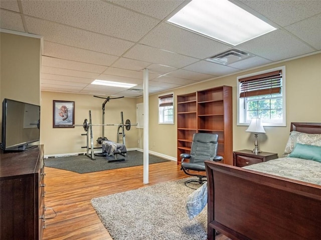 bedroom featuring baseboards, visible vents, a drop ceiling, and wood finished floors