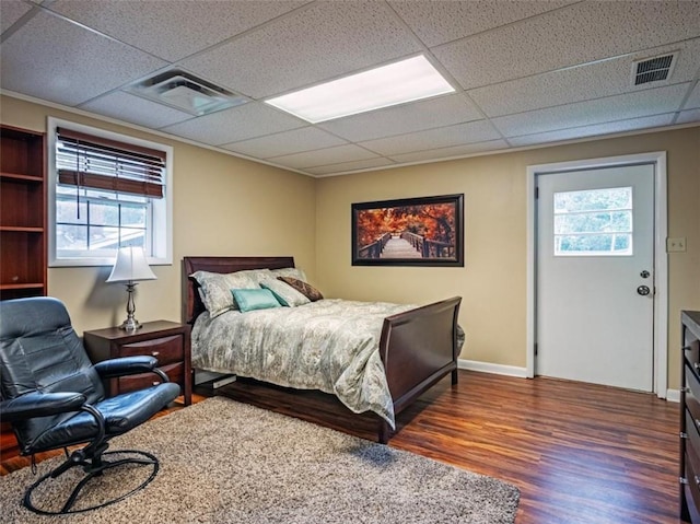 bedroom with a drop ceiling, wood finished floors, visible vents, and baseboards