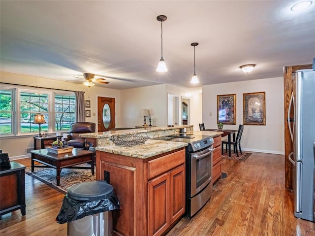 kitchen featuring brown cabinetry, light stone counters, wood finished floors, decorative light fixtures, and stainless steel appliances