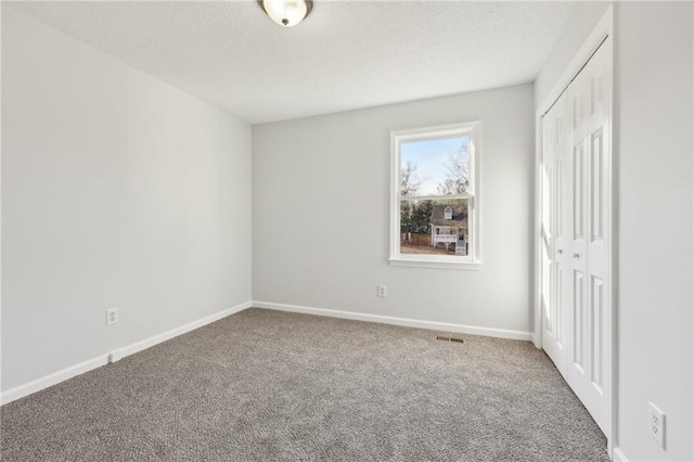 unfurnished bedroom featuring carpet floors, a closet, a textured ceiling, and baseboards