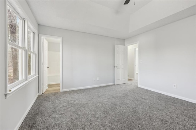 unfurnished bedroom featuring multiple windows, baseboards, a raised ceiling, and carpet flooring