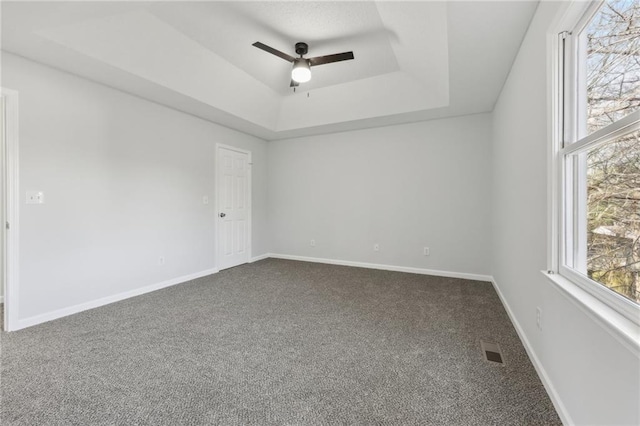 spare room with dark colored carpet, a raised ceiling, visible vents, and a healthy amount of sunlight