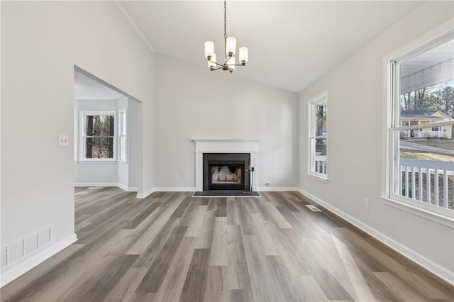 unfurnished living room featuring lofted ceiling, wood finished floors, a fireplace with flush hearth, visible vents, and baseboards