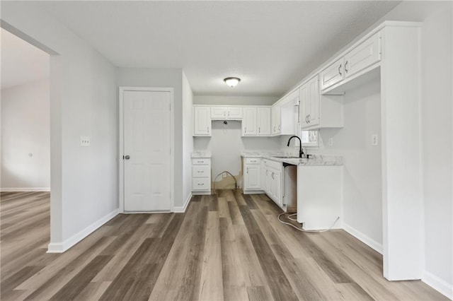 kitchen with white cabinets, a sink, baseboards, and wood finished floors