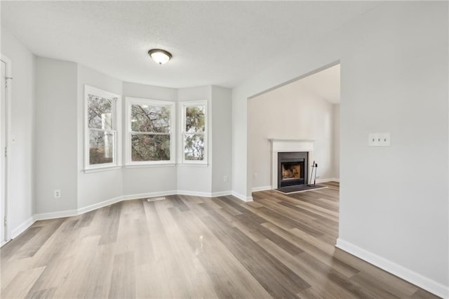 unfurnished living room featuring visible vents, a fireplace with flush hearth, a textured ceiling, wood finished floors, and baseboards