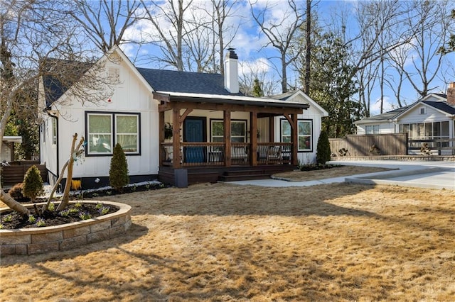 view of front of home featuring a chimney, roof with shingles, covered porch, fence, and a front lawn