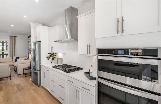 kitchen with white cabinetry, wall chimney exhaust hood, appliances with stainless steel finishes, and light wood-style flooring