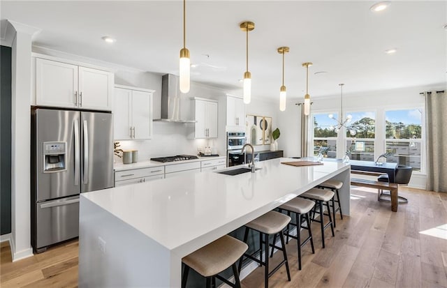 kitchen featuring a spacious island, appliances with stainless steel finishes, light wood-style floors, a sink, and wall chimney range hood