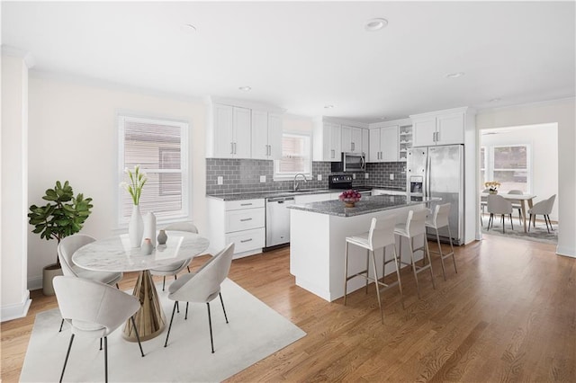 kitchen featuring dark stone countertops, appliances with stainless steel finishes, a center island, a healthy amount of sunlight, and white cabinets