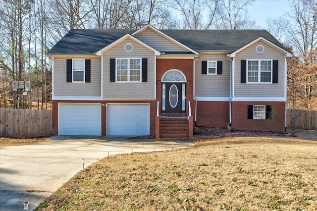 raised ranch with an attached garage, fence, brick siding, and driveway