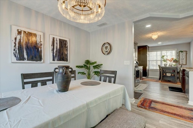 dining area featuring light wood finished floors, visible vents, baseboards, an inviting chandelier, and a textured ceiling