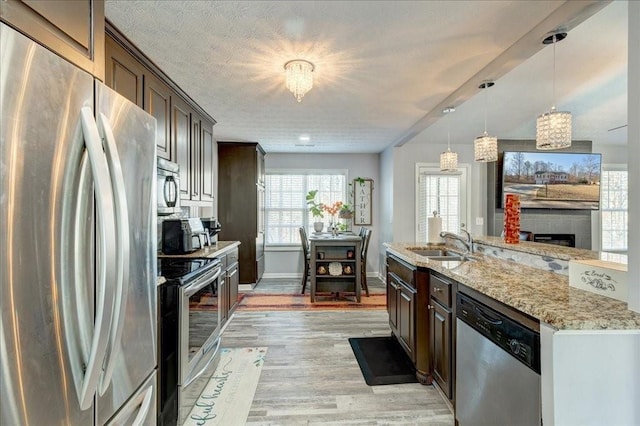 kitchen with dark brown cabinetry, appliances with stainless steel finishes, light wood-style floors, and a sink