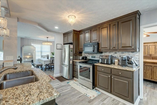 kitchen featuring light stone countertops, a chandelier, light wood-type flooring, stainless steel appliances, and a sink