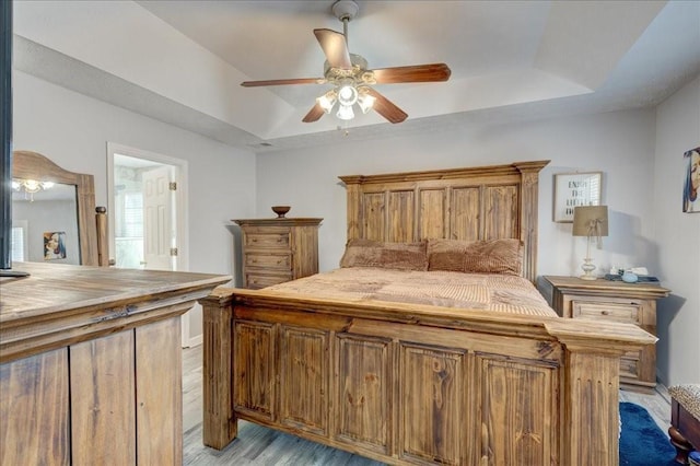 bedroom with a tray ceiling, a ceiling fan, and light wood finished floors