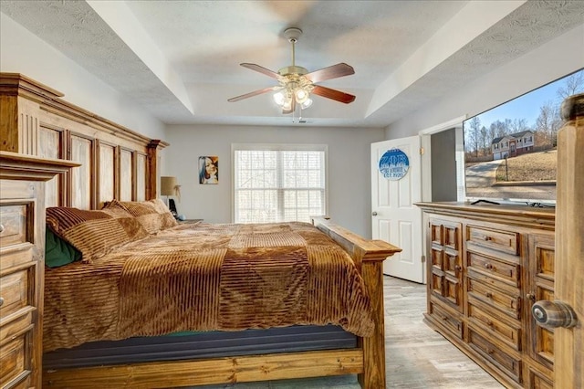 bedroom with a tray ceiling, light wood-style floors, and ceiling fan