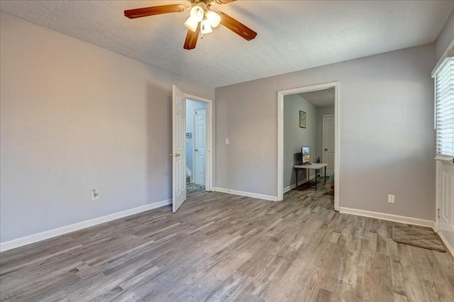 empty room with ceiling fan, baseboards, a textured ceiling, and wood finished floors