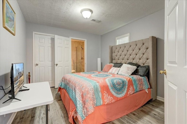 bedroom with connected bathroom, visible vents, a textured ceiling, and wood finished floors