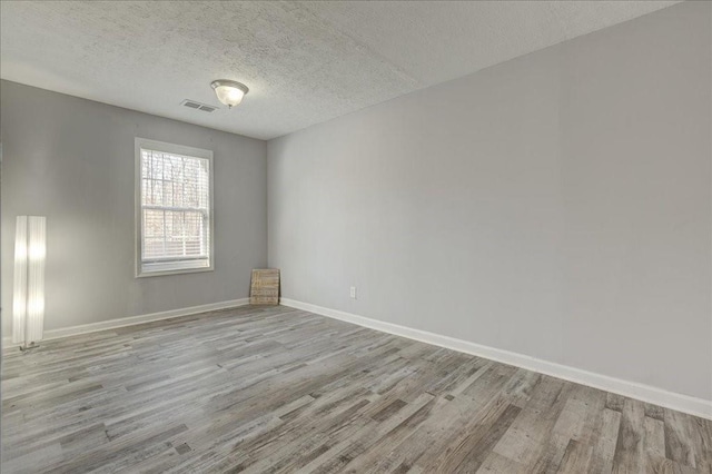 empty room featuring light wood-type flooring, visible vents, baseboards, and a textured ceiling