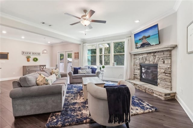 living area with crown molding, visible vents, a stone fireplace, wood finished floors, and baseboards