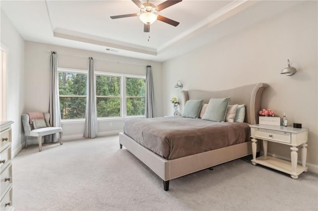 bedroom featuring light carpet, baseboards, a tray ceiling, and ceiling fan