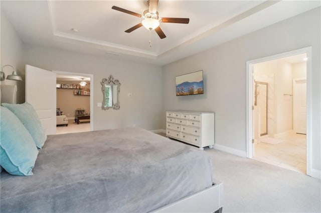 bedroom with light carpet, baseboards, ceiling fan, ensuite bathroom, and a tray ceiling