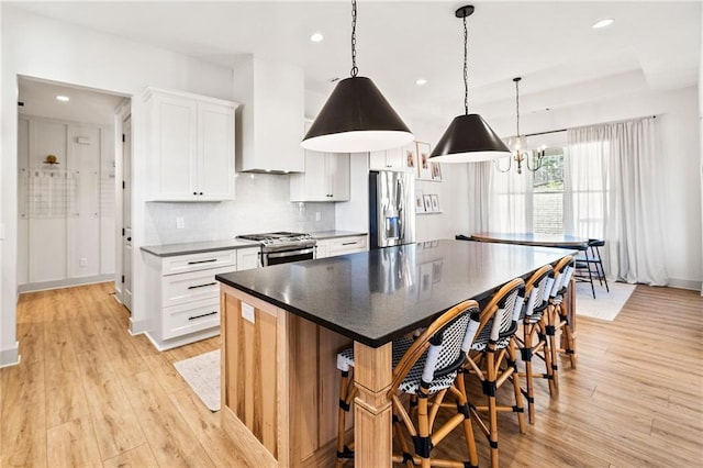 kitchen featuring wall chimney range hood, tasteful backsplash, white cabinetry, appliances with stainless steel finishes, and light wood finished floors