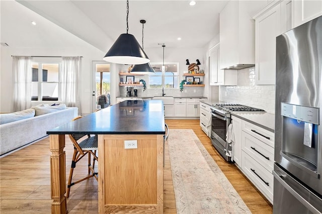 kitchen featuring a breakfast bar area, light wood-style floors, stainless steel appliances, wall chimney exhaust hood, and open shelves