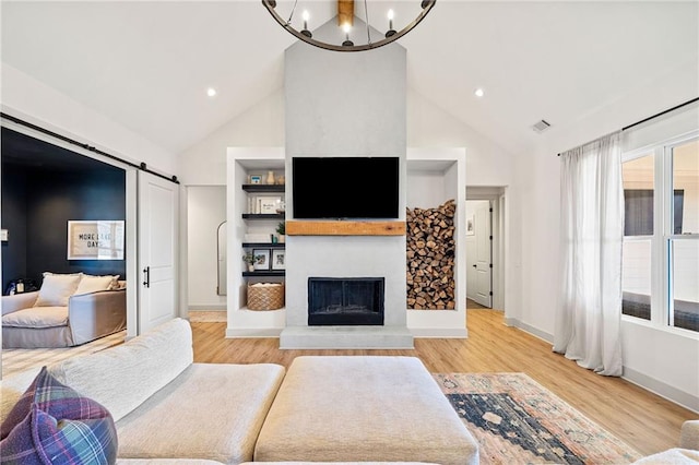 living area with visible vents, a fireplace with raised hearth, light wood-style flooring, plenty of natural light, and a barn door