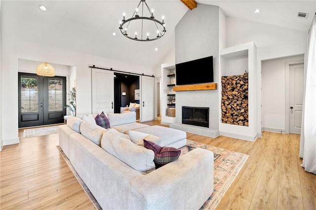 living area featuring visible vents, high vaulted ceiling, a fireplace with raised hearth, a barn door, and light wood-style floors