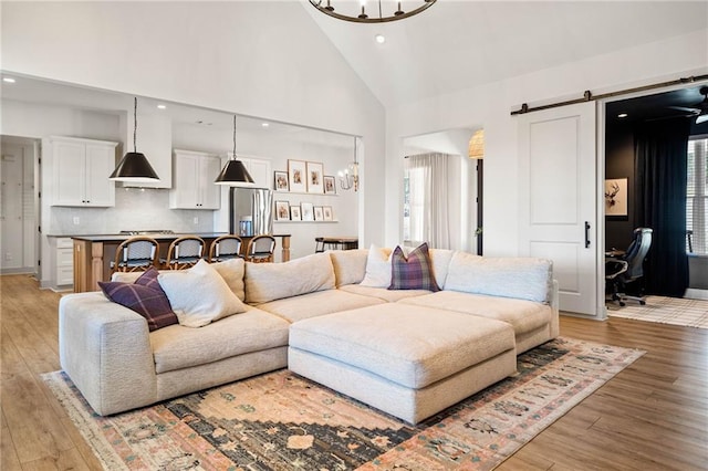 living area featuring high vaulted ceiling, recessed lighting, a barn door, a notable chandelier, and light wood-type flooring