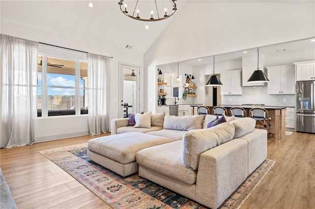 living area with light wood-style flooring, recessed lighting, ceiling fan with notable chandelier, and high vaulted ceiling