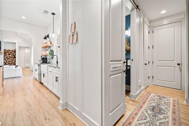 hallway featuring a barn door, light wood-style flooring, recessed lighting, and visible vents