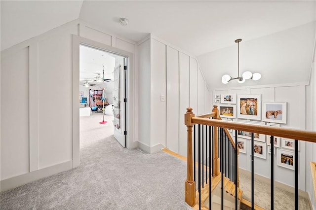 hallway featuring lofted ceiling, light carpet, a decorative wall, a notable chandelier, and an upstairs landing