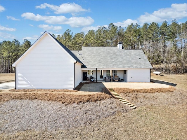 view of front facade with a shingled roof, a chimney, and a patio area