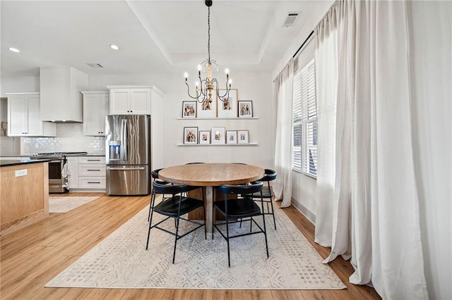 dining space with visible vents, baseboards, light wood-type flooring, a tray ceiling, and recessed lighting