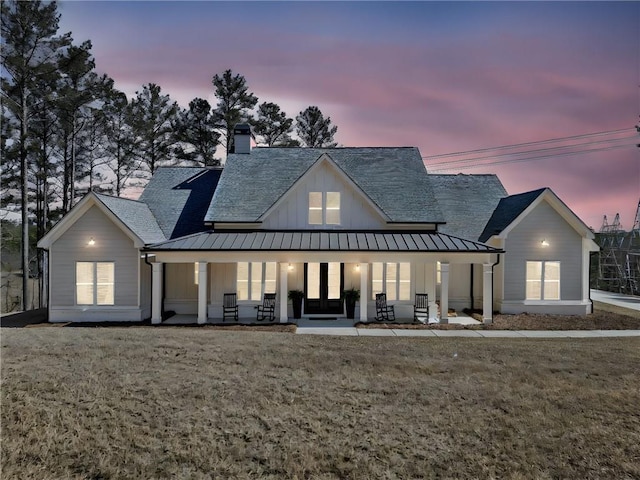 modern inspired farmhouse with a standing seam roof, board and batten siding, a front yard, metal roof, and a chimney