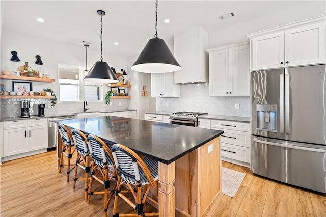 kitchen with visible vents, open shelves, light wood-style floors, appliances with stainless steel finishes, and wall chimney range hood