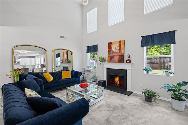 living room with a healthy amount of sunlight, a lit fireplace, a towering ceiling, visible vents, and marble finish floor