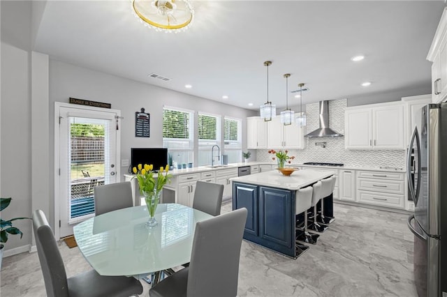 kitchen with visible vents, wall chimney range hood, light countertops, tasteful backsplash, and appliances with stainless steel finishes