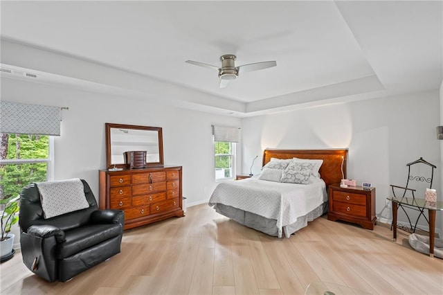 bedroom with a ceiling fan, a tray ceiling, visible vents, and light wood-style floors