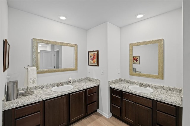 bathroom featuring baseboards, a sink, wood finished floors, and two vanities