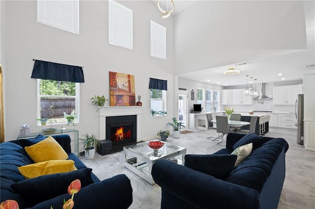living area featuring visible vents, a warm lit fireplace, a high ceiling, and a wealth of natural light