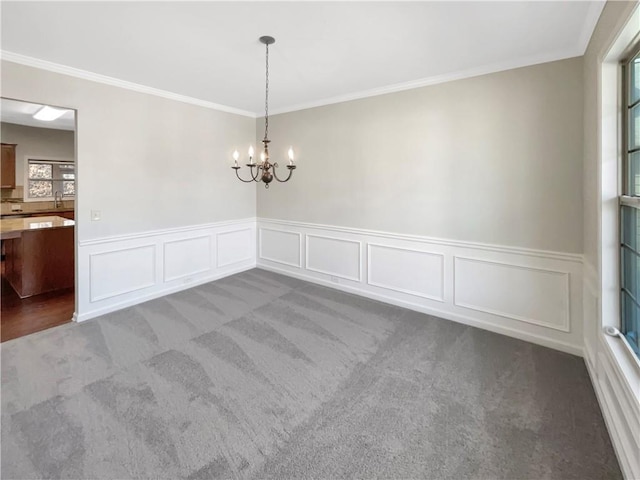 carpeted spare room with an inviting chandelier, crown molding, and wainscoting