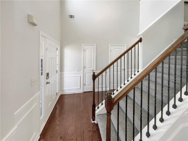 foyer with dark wood-style floors, a wainscoted wall, visible vents, a decorative wall, and stairs