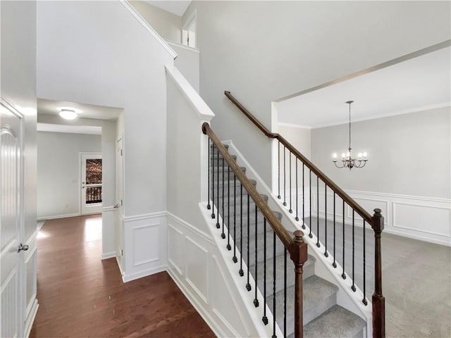 staircase with a towering ceiling, wood finished floors, an inviting chandelier, crown molding, and a decorative wall