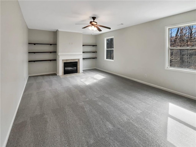 unfurnished living room with a fireplace with flush hearth, carpet, baseboards, and a ceiling fan