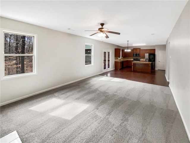 unfurnished living room with dark carpet, a wealth of natural light, and baseboards