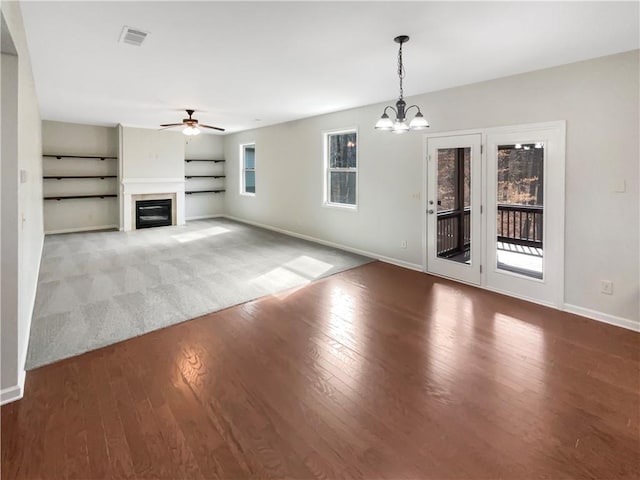 unfurnished living room with ceiling fan with notable chandelier, baseboards, wood finished floors, and a glass covered fireplace