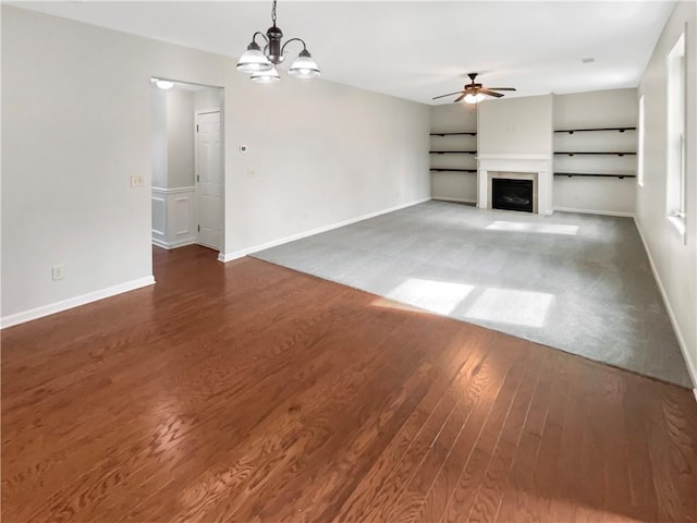 unfurnished living room with ceiling fan with notable chandelier, dark wood-style flooring, a fireplace, and baseboards